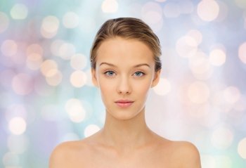 beauty, people and health concept - young woman face and shoulders over blue holidays lights background