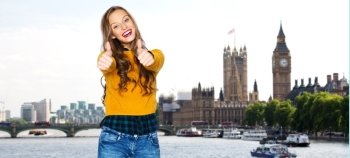 people, gesture, travel, tourism and fashion concept - happy young woman or teen girl in casual clothes showing thumbs up over thames river bridge and big ben in london city background