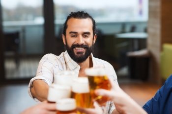 leisure, drinks, celebration, people and holidays concept - smiling man clinking beer glass with friends at restaurant