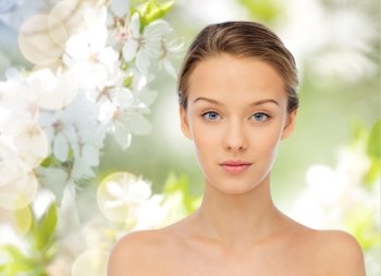 beauty, people, organic, eco and health concept - young woman face and shoulders over green natural background with cherry blossoms