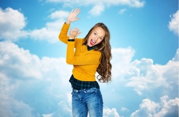 people, style and fashion concept - happy young woman or teen girl in casual clothes having fun and applauding over blue sky and clouds background