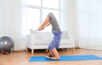 fitness, sport, people and healthy lifestyle concept - woman making yoga in headstand pose on mat