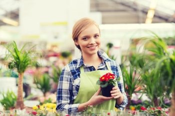 people, gardening and profession concept - happy woman or gardener holding flowers in greenhouse