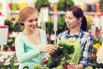 people, gardening, shopping, sale and consumerism concept - happy gardener helping woman with choosing flowers in greenhouse