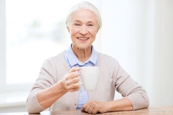 age, drink and people concept - happy smiling senior woman with cup of tea or coffee at home