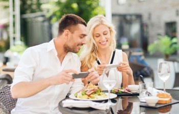 love, date, technology, people and relations concept - happy couple with smatphone taking picture of food at restaurant