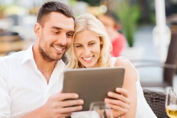 love, dating, people, technology and holidays concept - happy couple with tablet pc computer at restaurant lounge or terrace