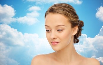 beauty, people and health concept - smiling young woman face and shoulders over blue sky and clouds background