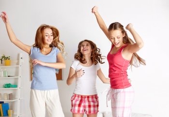 friendship, people and pajama party concept - happy friends or teenage girls having fun and jumping on bed at home