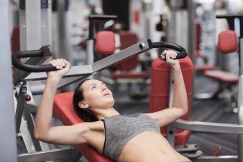 sport, fitness, lifestyle and people concept - young woman flexing muscles on gym machine