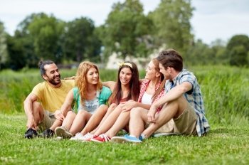 friendship, leisure, summer and people concept - group of smiling friends sitting on grass and talking outdoors