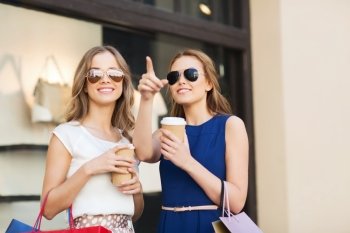sale, consumerism and people concept - happy young women with shopping bags and coffee paper cup pointing finger at shop window in city