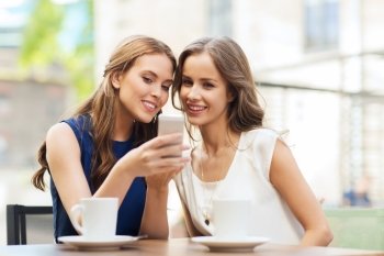 technology, lifestyle, friendship and people concept - happy young women or teenage girls with smartphone and coffee cups at outdoor cafe