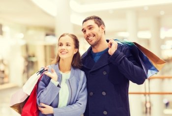 sale, consumerism and people concept - happy young couple with shopping bags walking in mall