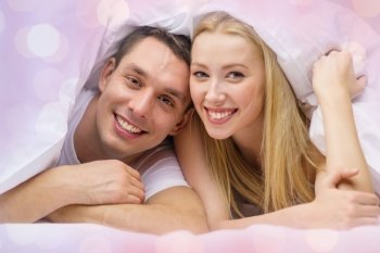 love, valentines day and people concept - happy couple in bed over holidays lights background