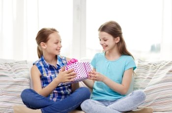 people, children, holidays, friends and friendship concept - happy little girls with birthday present sitting on sofa at home