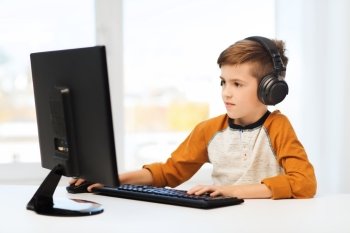 leisure, education, children, technology and people concept - happy boy with computer and headphones typing on keyboard or playing video game at home