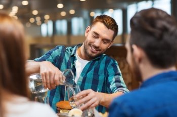 leisure, people and holidays concept - smiling man with friends pouring water from jug at restaurant