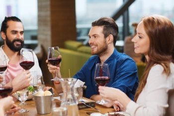 leisure, food and drinks, celebration people and holidays concept - smiling friends having dinner and drinking red wine at restaurant