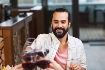 leisure, eating, food and drinks, people and holidays concept - happy man with friends clinking glasses of wine at restaurant