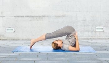 fitness, sport, people and healthy lifestyle concept - woman making yoga in plow pose on mat over urban street background