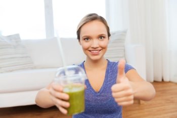 people, diet  and healthy lifestyle concept - happy woman with cup of smoothie at home and showing thumbs up