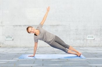 fitness, sport, people and healthy lifestyle concept - woman making yoga in side plank pose on mat over urban street background