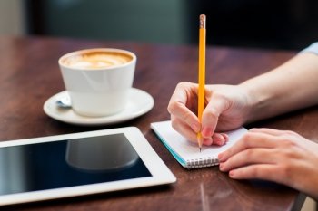 business, education, people, technology and lifestyle concept - close up of woman hands writing to notebook by pencil and tablet pc computer with coffee