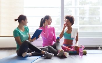 fitness, sport, technology and lifestyle concept - group of happy women with smartphone, earphones and tablet pc computer listening to music in gym
