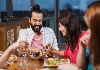 leisure, eating, food, people and holidays concept - smiling friends having dinner and tasting each other dish at restaurant