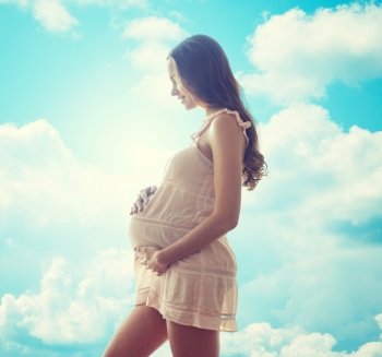 pregnancy, motherhood, people and expectation concept - happy pregnant woman in chemise over blue sky and clouds background