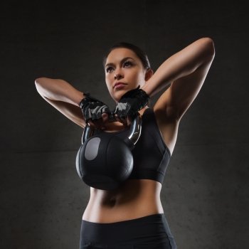 fitness, sport, exercising, weightlifting and people concept - young woman flexing muscles with kettlebell in gym