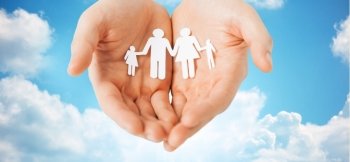 people, values and happiness concept - close up of man cupped hands showing paper family cutout over blue sky and clouds background