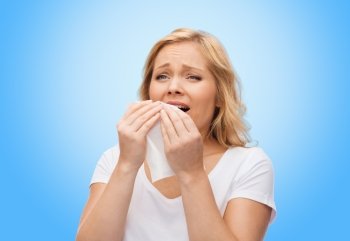 people, healthcare, rhinitis, cold and allergy concept - unhappy woman with paper napkin sneezing over blue background