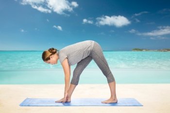 fitness, sport, people and healthy lifestyle concept - woman making yoga intense stretch pose on mat over beach background