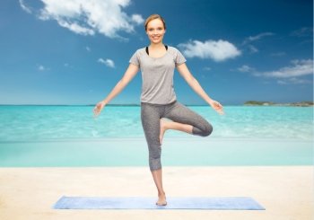 fitness, sport, people and healthy lifestyle concept - woman making yoga in tree pose on mat over beach background