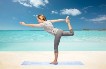 fitness, sport, people and healthy lifestyle concept - woman making yoga in lord of the dance pose on mat over beach background