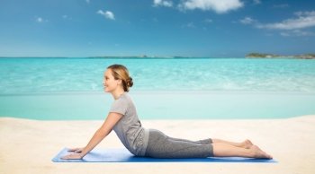 fitness, sport, people and healthy lifestyle concept - woman making yoga in dog pose on mat over sea and sky background