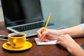 business, education, people, technology and lifestyle concept - close up of woman writing to notebook with pencil