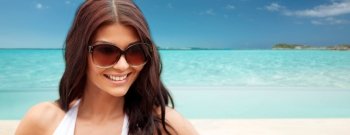 summer vacation, tourism, travel, holidays and people concept -face of smiling young woman with sunglasses over tropical beach background