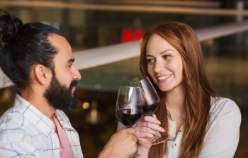 leisure, eating, food and drinks, people and holidays concept - smiling couple celebrating anniversary and clinking red wine glasses at restaurant