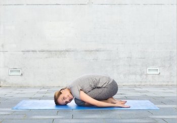 fitness, sport, people and healthy lifestyle concept - happy woman making yoga in child pose on mat over urban street background
