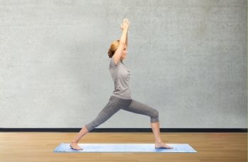 fitness, sport, people and healthy lifestyle concept - woman making yoga warrior pose on mat over gym room background