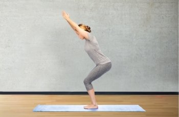fitness, sport, people and healthy lifestyle concept - woman making yoga in chair pose on mat over gym room background