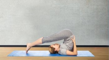 fitness, sport, people and healthy lifestyle concept - woman making yoga in plow pose on mat over gym room background