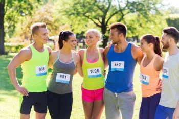 fitness, sport, marathon, friendship and healthy lifestyle concept - group of happy teenage friends or sportsmen couple with racing badge numbers outdoors