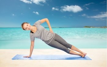 fitness, sport, people and healthy lifestyle concept - woman making yoga in side plank pose on mat over beach background