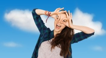 people and teens concept - happy smiling pretty teenage girl making face and having fun over blue sky and clouds background. happy teenage girl making face and having fun