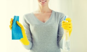 people, housework and housekeeping concept - close up of happy woman with cloth and cleanser spray at home