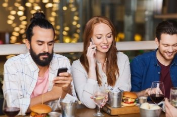 leisure, technology, lifestyle and people concept - happy friends with smartphones calling and texting at dinner in restaurant